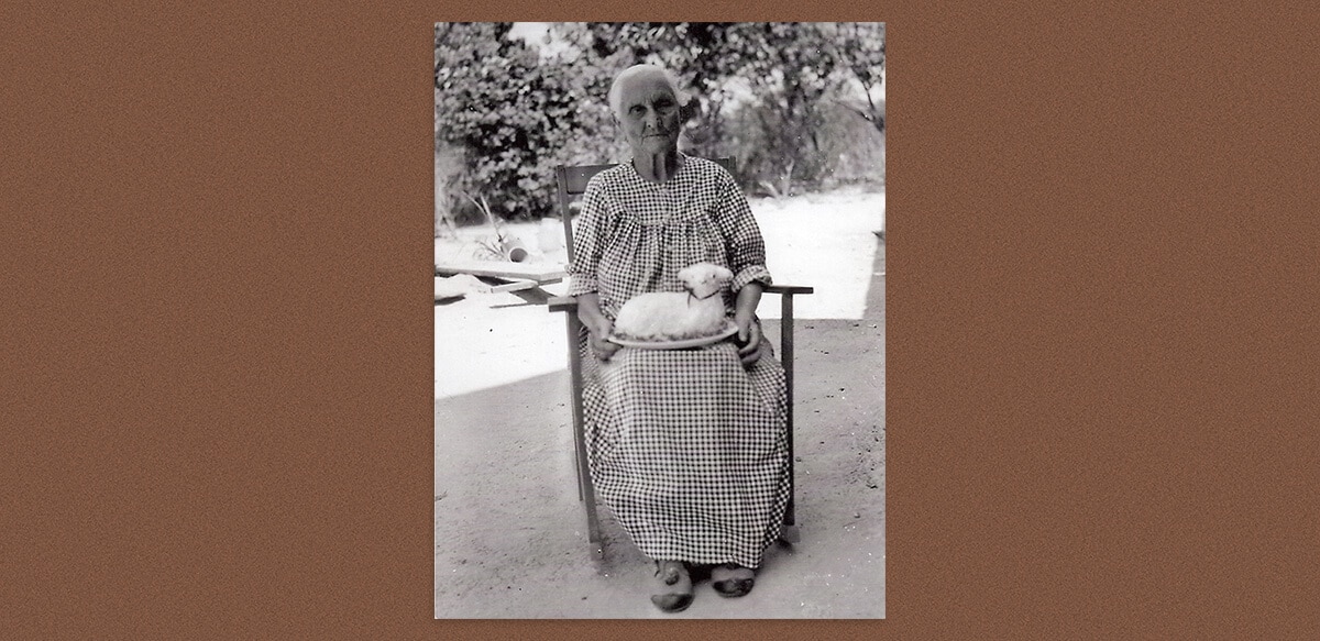 Old woman sitting on a chair outside, with a lamb cake in her lap