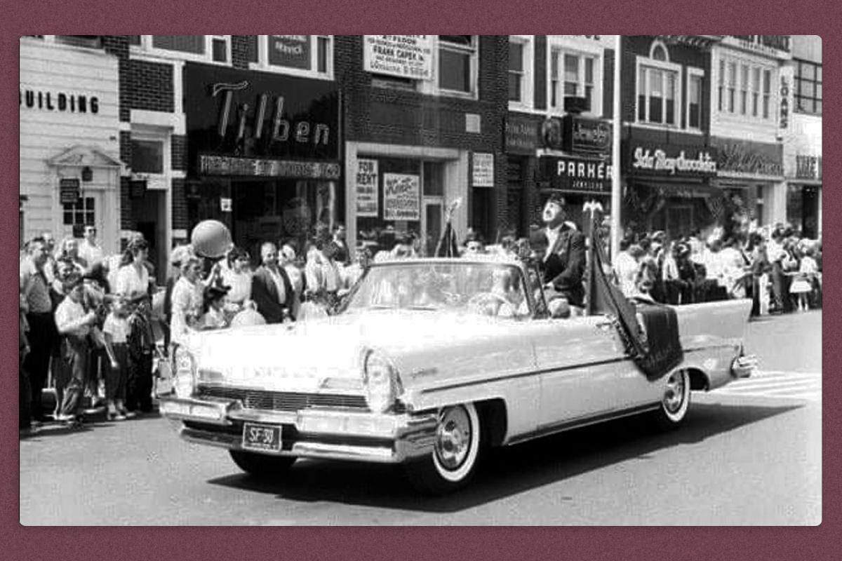 A open-top convertible driving in a parade, with Michael Valente on board