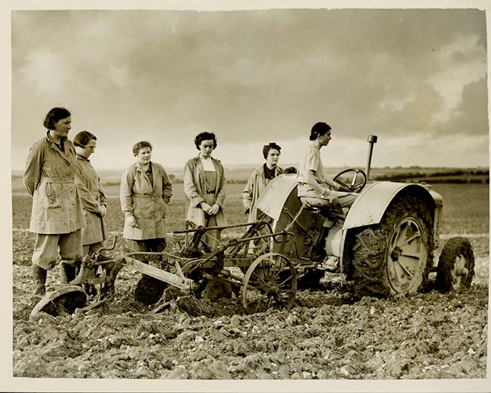 Members of the Women's Land Army stand round their tractor plough